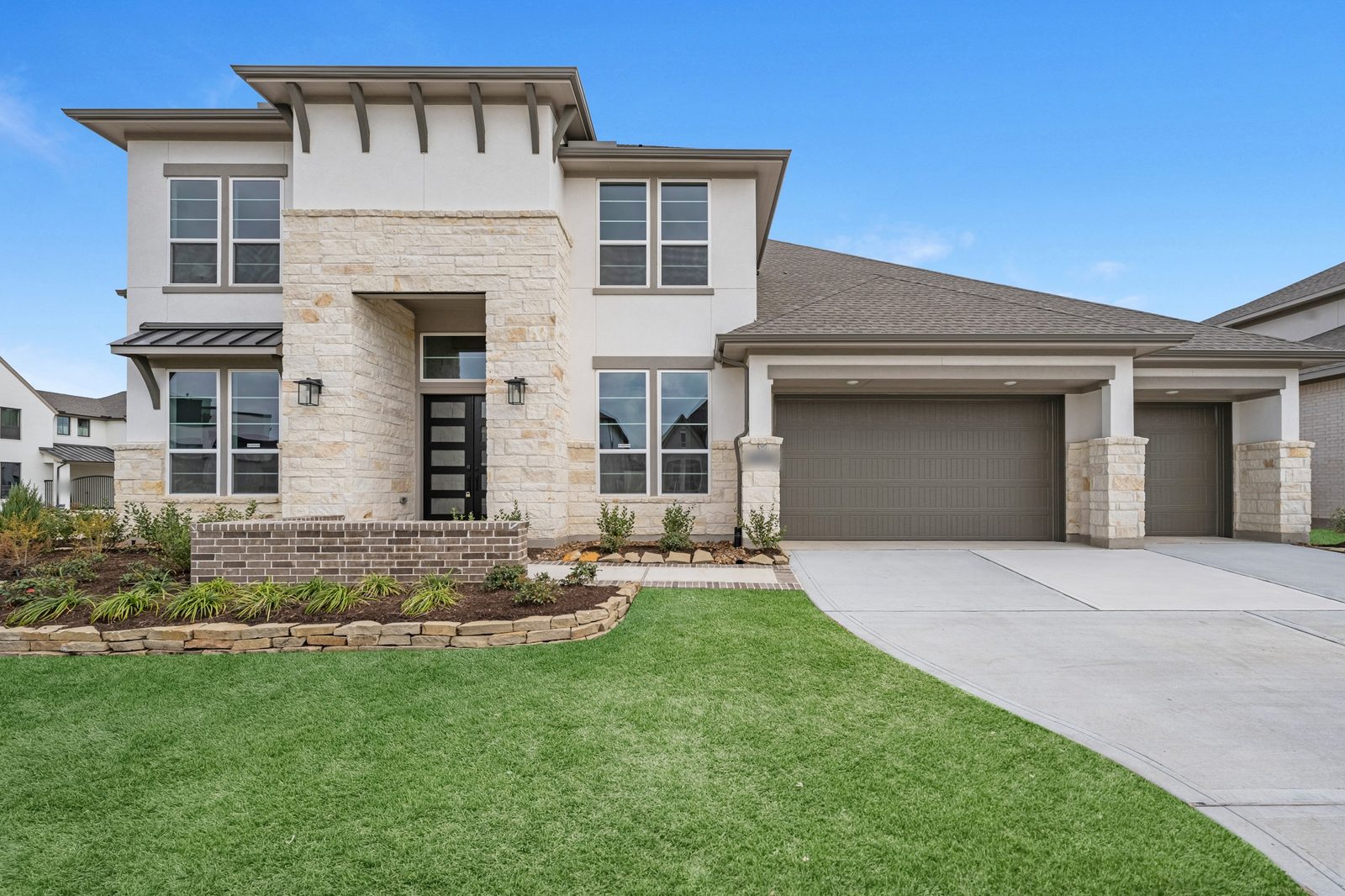 Two-story new-construction home with a cream stone entry tower and a three-car garage under a blue sky