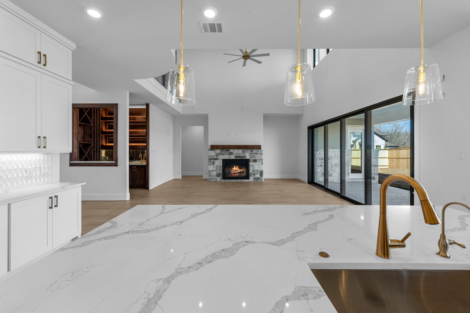 New-construction kitchen with a marble island, brass pendants and a stone fireplace beyond