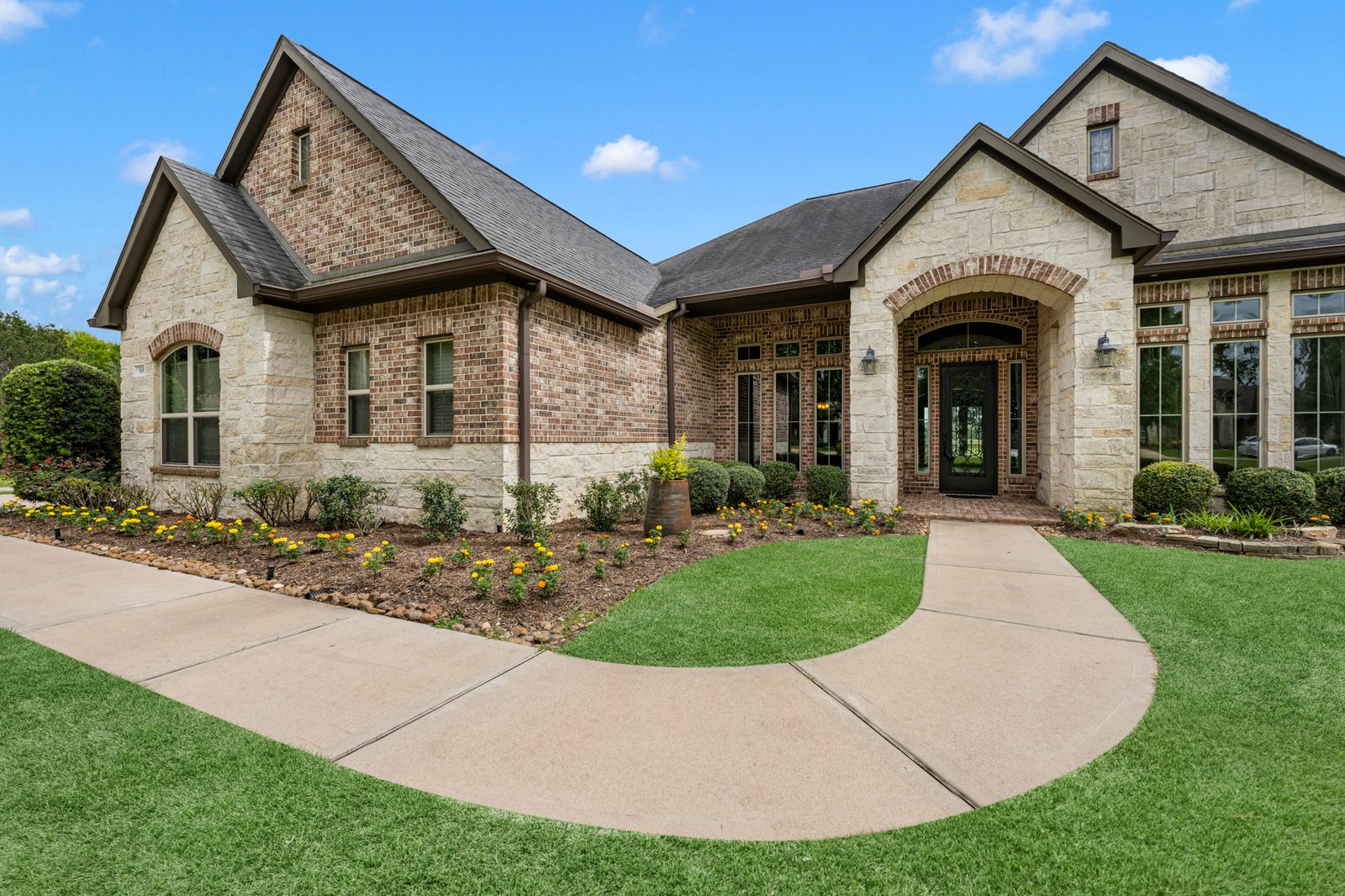 Stone and brick home with a curved front walkway and fresh landscaping on a sunny day