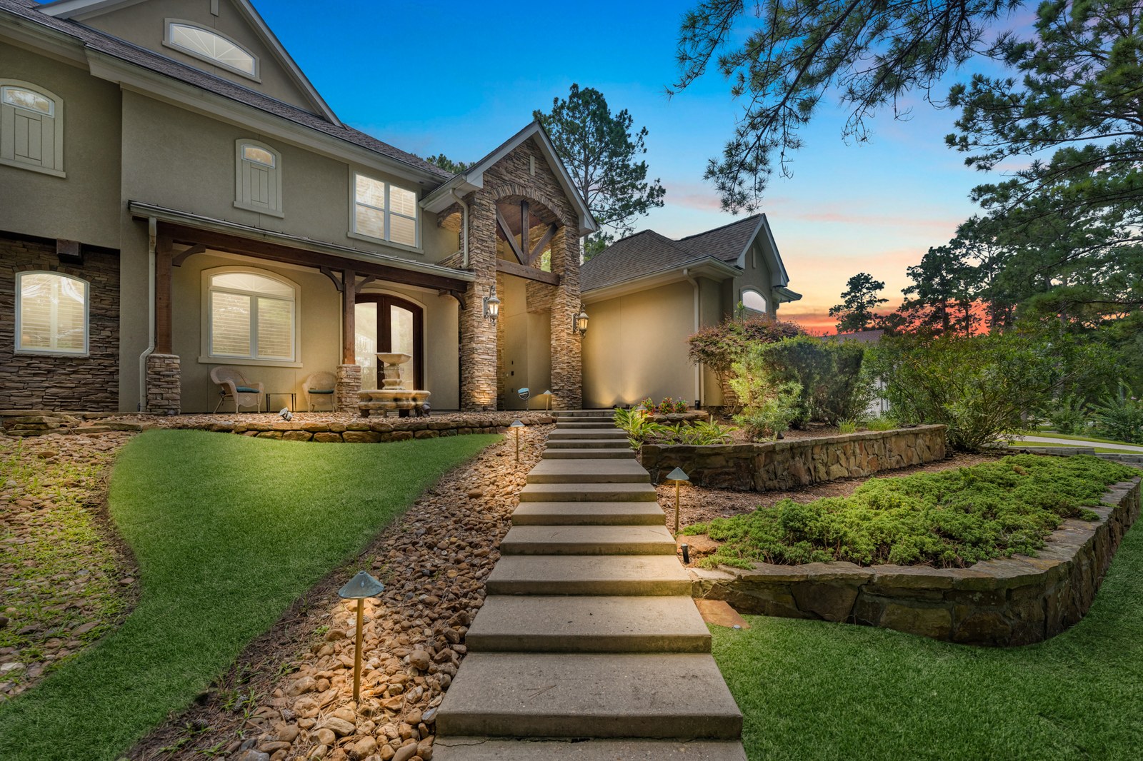 Virtual twilight of a stone and stucco home with lit path lights and stone steps