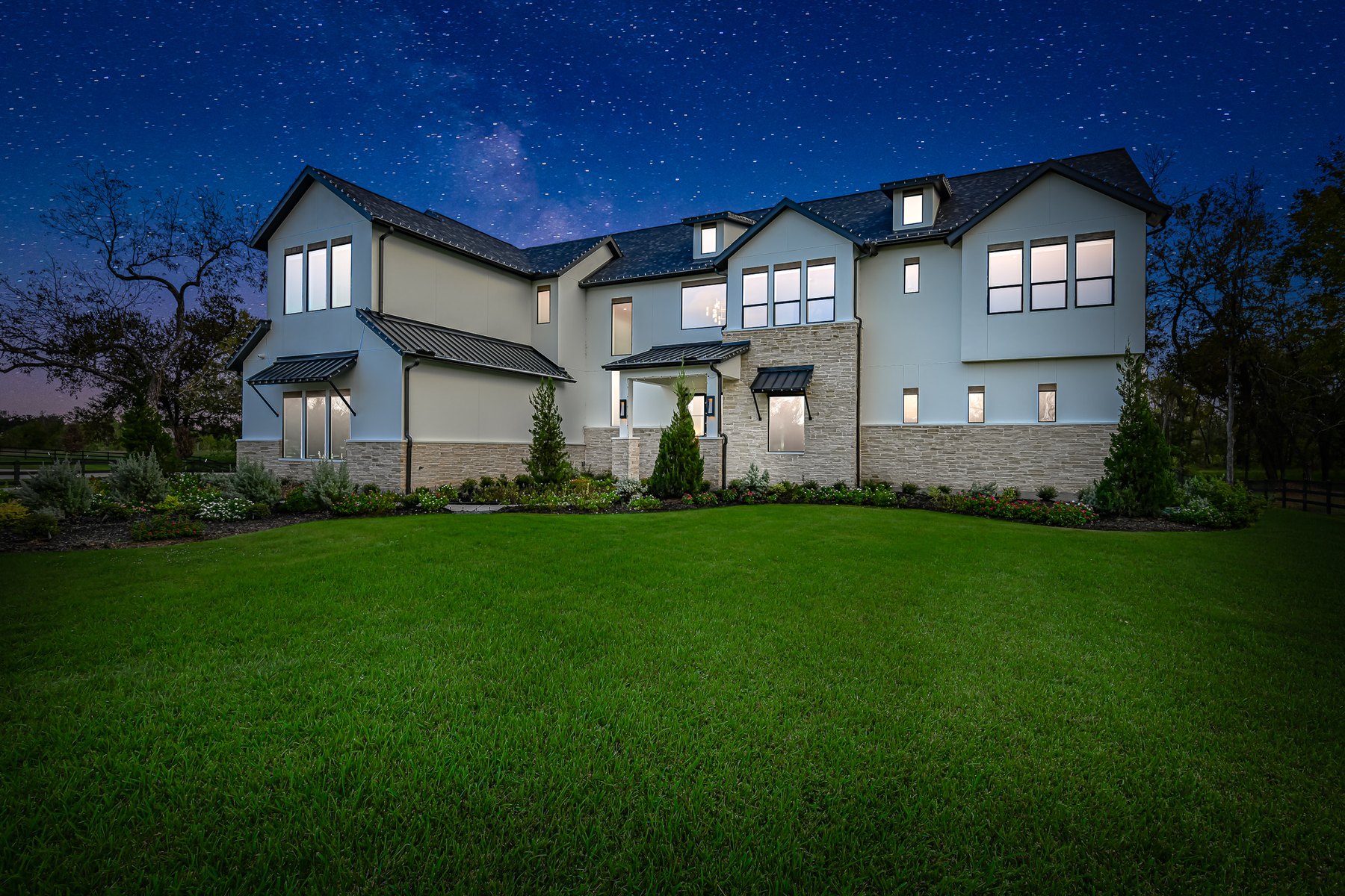 Virtual twilight of a two-story home under a starry night sky with every window lit